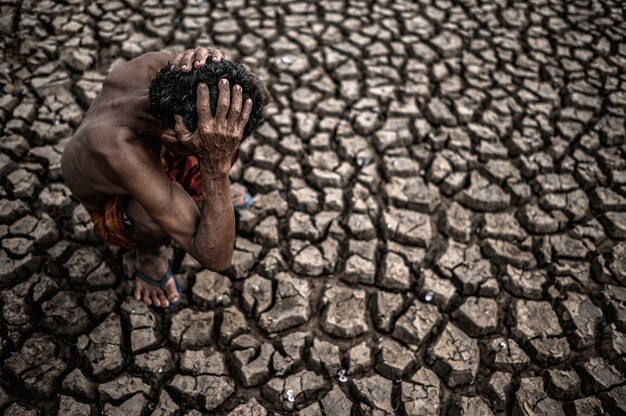 An elderly man sat bent his knees at a dry floor and his hands held his head, global warming