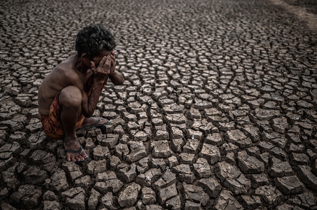 An elderly man sat bent his knees at dry ground and hands closed on his face, global warming