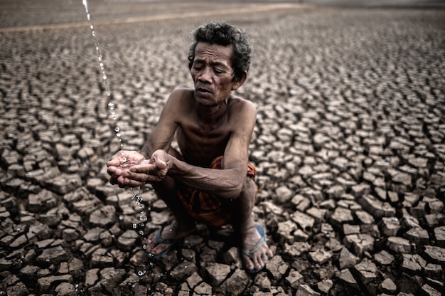 Un uomo anziano seduto in contatto con la pioggia nella stagione secca, riscaldamento globale, messa a fuoco selettiva