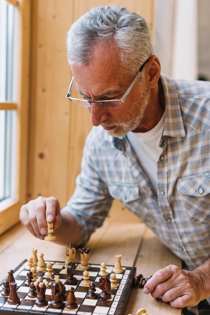 An elderly man wearing spectacles playing chess on window sill