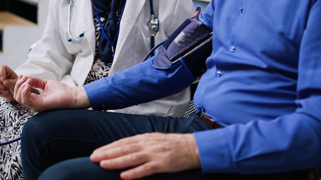 Free photo elderly medic using medical tonometer to measure patient pulse pressure and hypertension, doing cardiology examination in hospital waiting room. senior man attending checkup visit. medicine concept