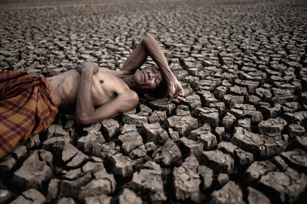 Elderly men lay flat on their hands, on the stomach and forehead, on dry soil, global warming.