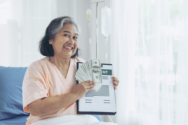 Free photo elderly patients injury  woman on patient's bed in hospital  holding us dollar bills feel happy from getting insurance money from insurance companies