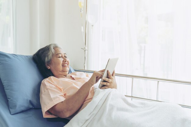Пожилые пожилые пациенты в больничной койке, использующие умный телефонный звонок, чтобы родственники-потомки чувствовали счастье - старшая женская медицинская и медицинская концепция
