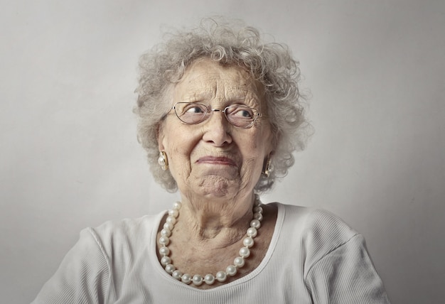 Elderly woman against a white wall with a worried look on her face