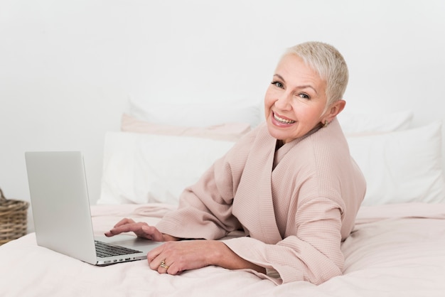 Free photo elderly woman in bathrobe smiling and posing with laptop in bed