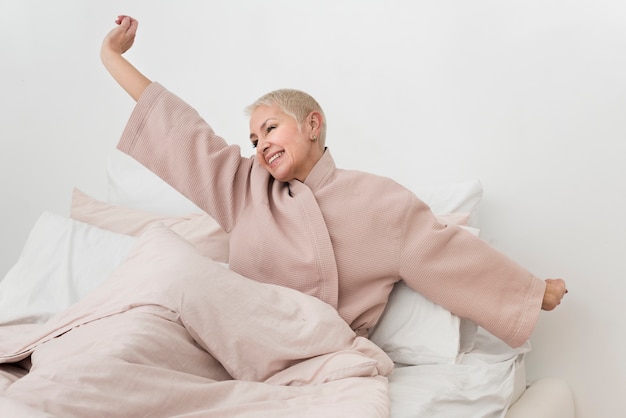 Пожилая женщина в халате растягивается в постели