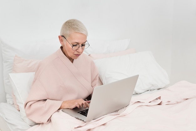 Free photo elderly woman in bathrobe working on laptop in bed