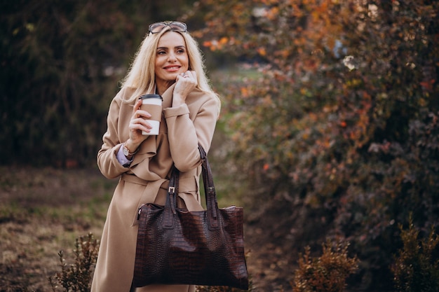 秋の公園の外でコーヒーを飲む高齢者の女性