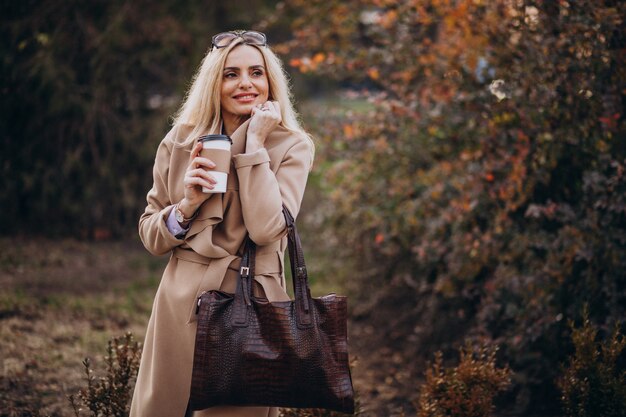 Пожилая женщина пьет кофе у осеннего парка