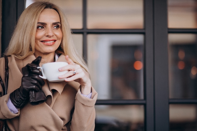 Donna anziana che beve caffè fuori dal bar