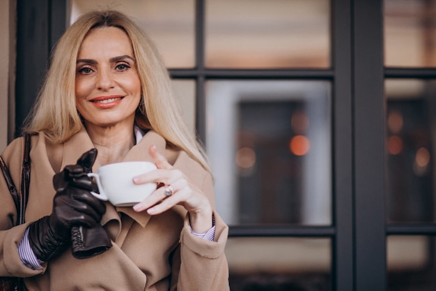 カフェの外でコーヒーを飲む高齢者の女性