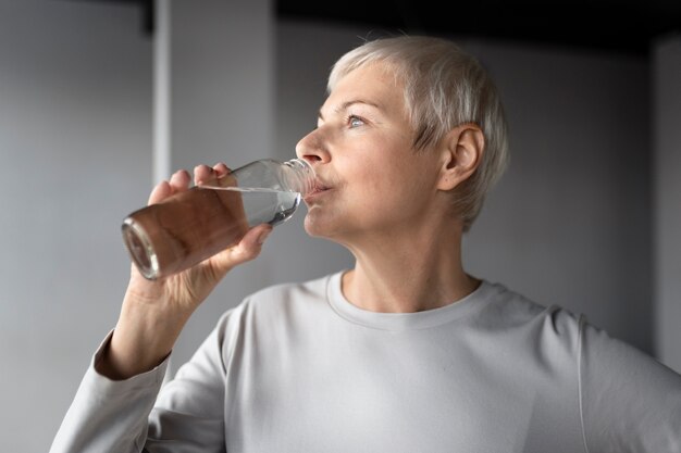Elderly woman drinking water after workout at the gym