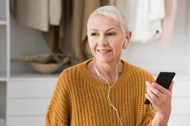 高齢者の女性がヘッドフォンで音楽を聴くとスマートフォンを保持