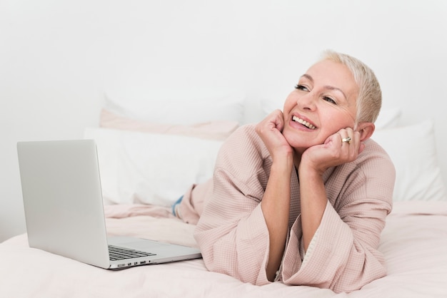 Elderly woman posing in bathrobe with laptop in bed
