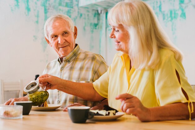 Elderly woman pouring tea to gray haired man