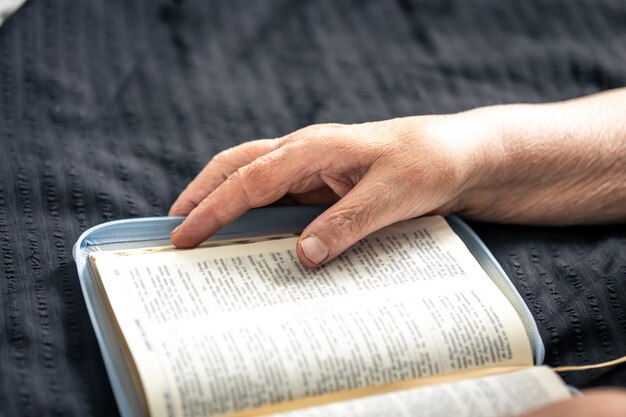 An elderly woman reads a book of the bible hands and closeup