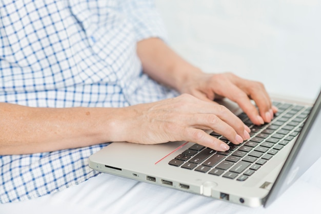 Рука пожилой женщины печатает на переносном ноутбуке