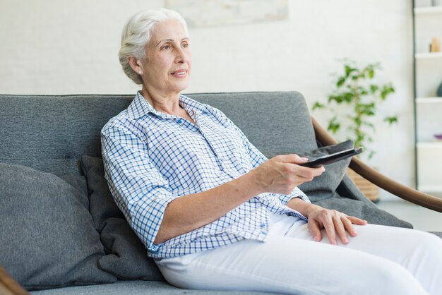 An elderly woman watching television using remote