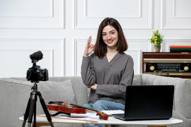 Elearning cute young beautiful girl remotely at home giving violin classes saying hi