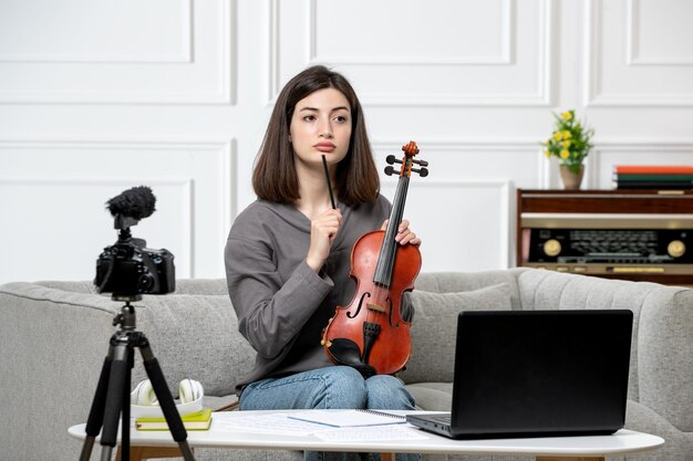 自宅でバイオリンのクラスをリモートで行うeラーニング若いかわいい美しい女の子がカメラで混乱している