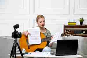 Бесплатное фото Электронное обучение молодой милой красивой девушки, дистанционно дающей уроки игры на гитаре дома с нотами