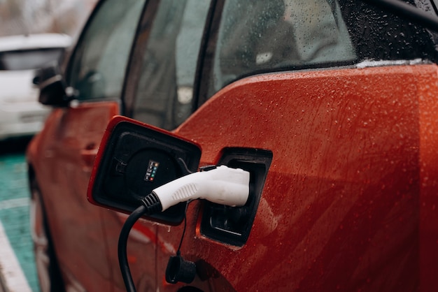 Foto gratuita auto elettrica con cavo di alimentazione collegato, vista serale della città.