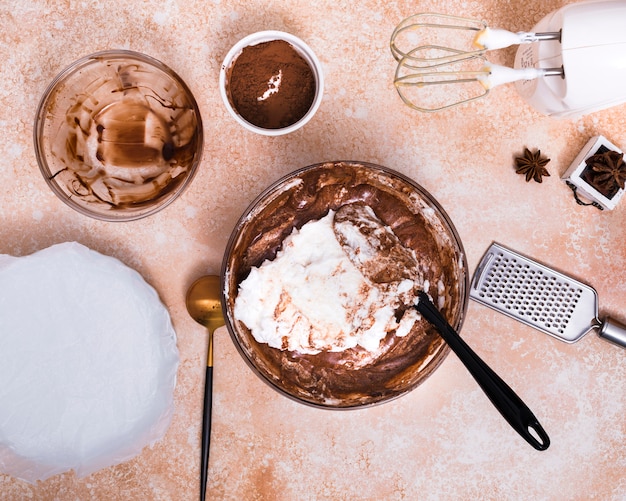 Electric food mixer; hand grater; star anise; cocoa powder and cake dough on brown textured background