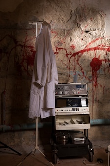고문이나 무서운 할로윈 테마에 대한 개념을 위해 피 묻은 벽으로 옷걸이에 걸려 있는 의료 가운 근처의 전기 충격 장치