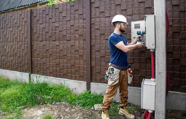 無料写真 仕事中の電気技師ビルダーは、産業用配電盤の胴体の電線のケーブル接続を調べます。電気技師のツールを使用したオーバーオールのプロ。