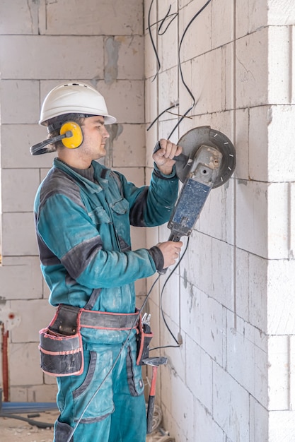 An electrician construction worker in a protective helmet at a work facility works with a grinder.