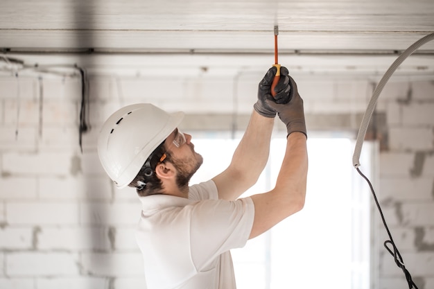 Foto gratuita installatore di elettricista con uno strumento nelle sue mani, lavorando con il cavo in cantiere.