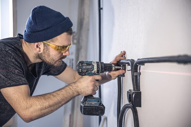 An electrician is mounting electric sockets on the white wall indoors