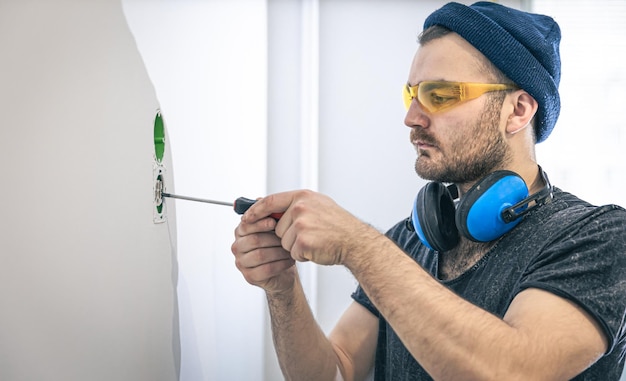 An electrician is mounting electric sockets on the white wall indoors