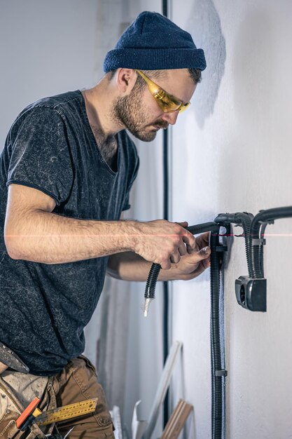 電気技師が屋内の白い壁に電気ソケットを取り付けています