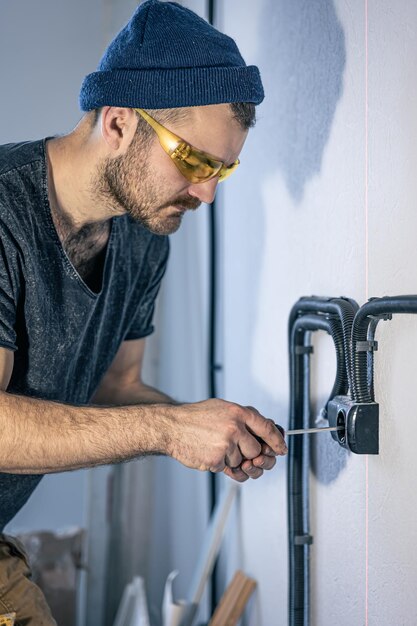 An electrician is mounting electric sockets on the white wall indoors