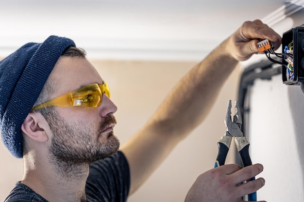 An electrician is mounting electric sockets on the white wall indoors