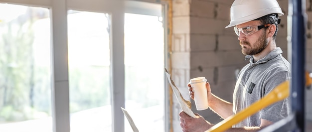 Free photo an electrician is studying a construction drawing with a coffee in his hand