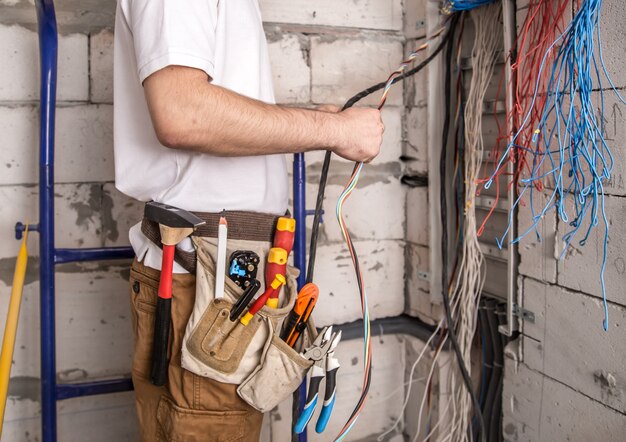 ボードの近くでワイヤーを使って作業する電気技師。電気の設置と接続。