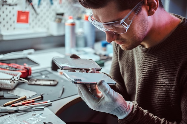 Electronic technician holds two identical smartphones for comparison, in one hand broken and in another new