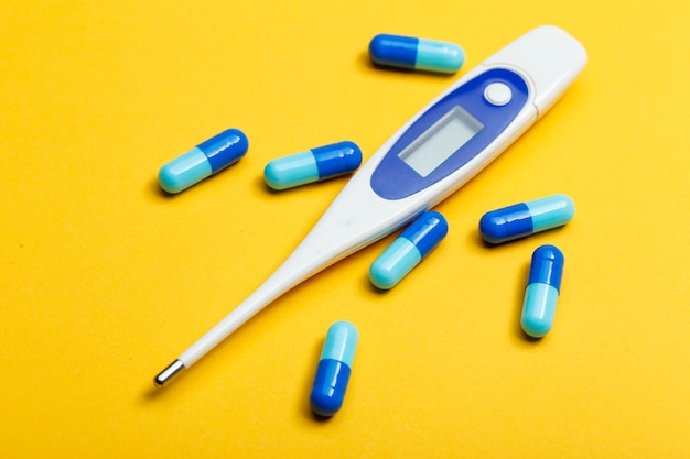 electronic thermometer and blue capsules on yellow background