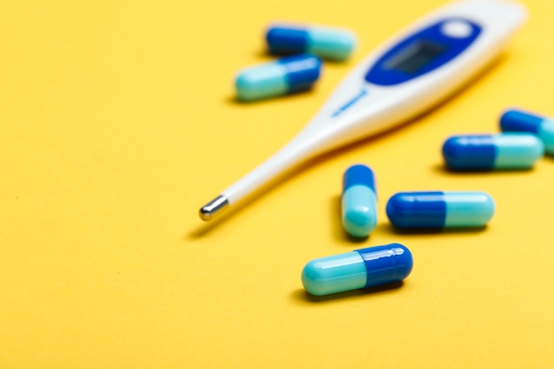 electronic thermometer and blue capsules on yellow background