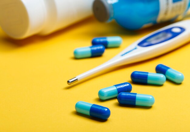 electronic thermometer and blue capsules on yellow background