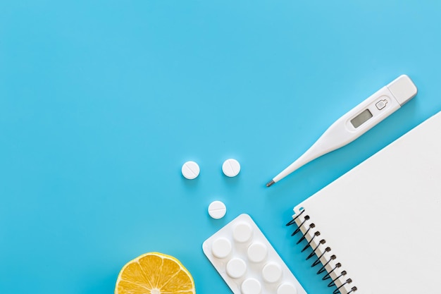 Free photo electronic thermometer pills and notepad on a blue background flat lay