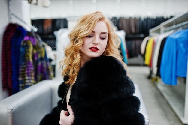 毛皮のコートと革のジャケットの店で毛皮のコートの優雅なブロンドの女の子
