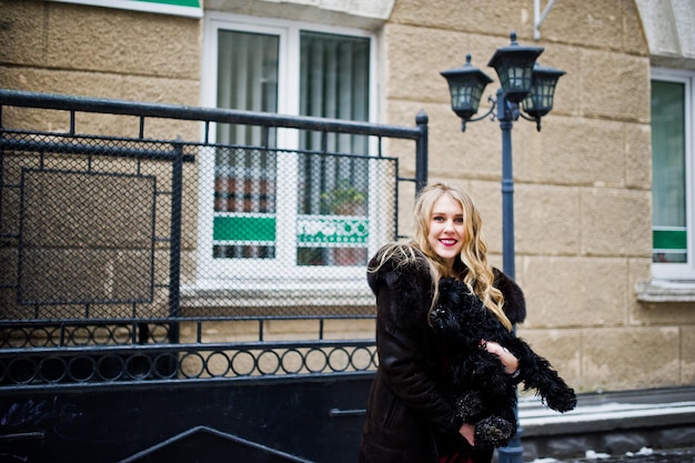 Elegance blonde girl in red evening dress and fur coat at streets of city in winter day