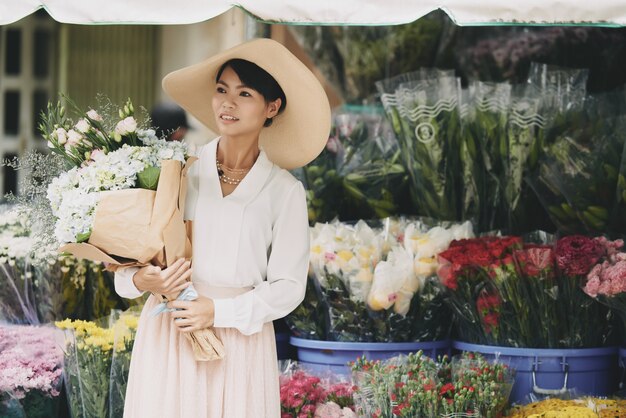 フラワーショップの前の通りで待っている大きな花束とエレガントなアジアの女性