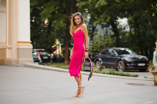 Elegant attractive woman wearing pink sexy summer dress walking in street holding handbag