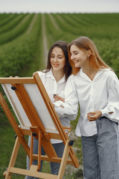 Free photo elegant and beautiful girls painting in a field