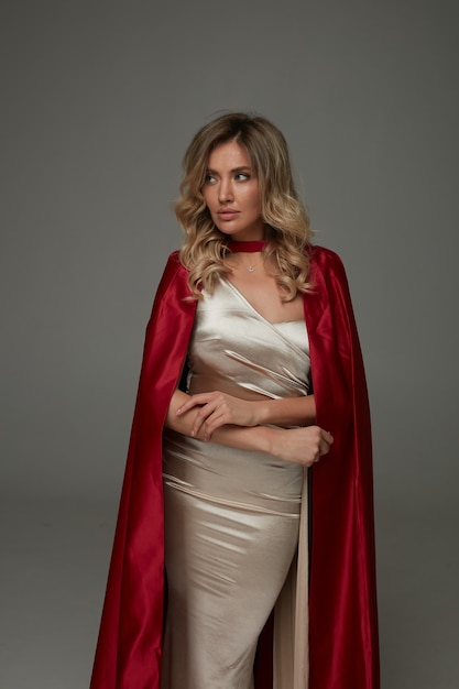 Elegante donna bionda in abito lungo lucido e mantello di seta rossa